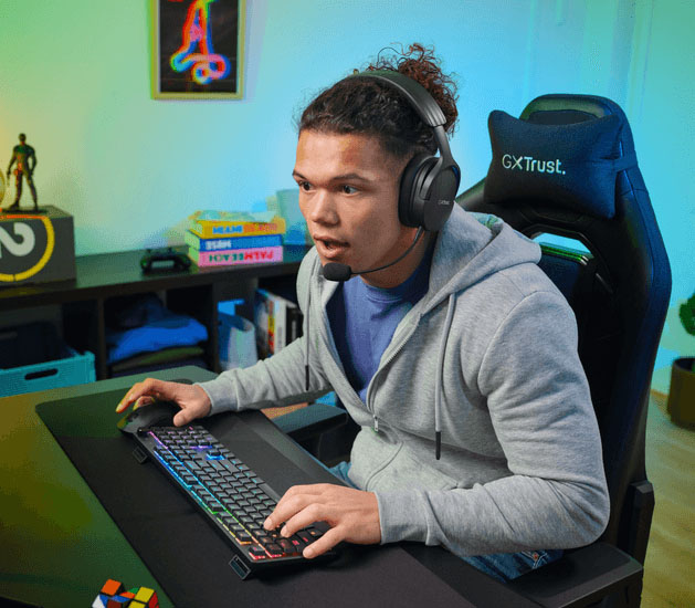 Persona jugando en PC con teclado mecánico inalámbrico Trust GXT 868 Torix con iluminación RGB y auriculares con micrófono