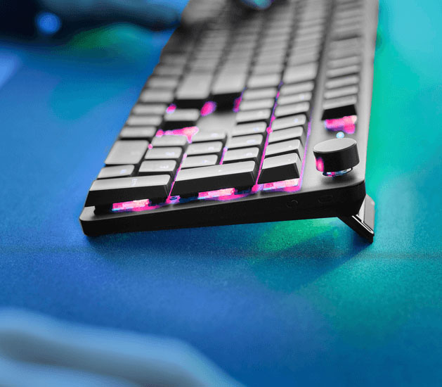 Detalle en ángulo del teclado Trust GXT 868 Torix con iluminación RGB, perilla lateral y patas elevadoras desplegadas