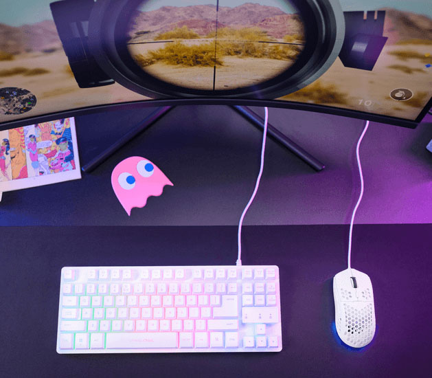 Mouse gaming Trust GXT 928W Helox ultraliviano con iluminación RGB sobre un escritorio gamer junto a un teclado compacto y un monitor curvo