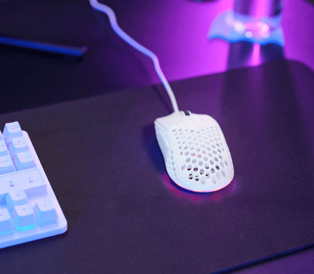 Mouse gaming Trust GXT 928W Helox ultraliviano con diseño perforado e iluminación RGB sobre un escritorio gamer