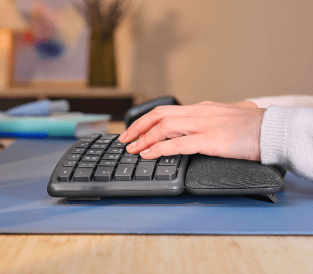 Vista lateral de una mano apoyada sobre el teclado ergonómico Trust Keyra con reposamanos acolchado