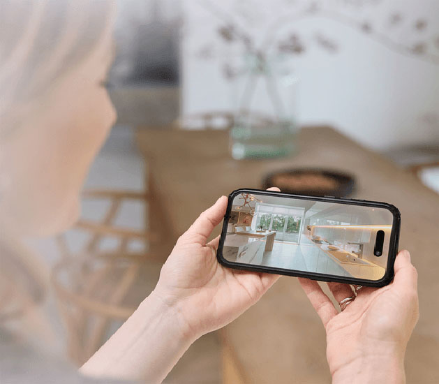Persona sosteniendo un teléfono móvil y mirando una transmisión de video en vivo de una cocina moderna.
