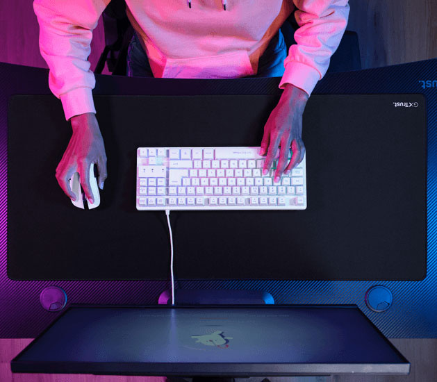 Vista superior de un escritorio con un mousepad XXL negro, teclado y mouse, con una persona apoyando las manos sobre los periféricos