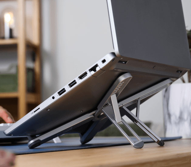 Notebook apoyada sobre el soporte plegable de aluminio Macy de Trust, mostrando su diseño compacto y resistente en un escritorio de trabajo moderno.