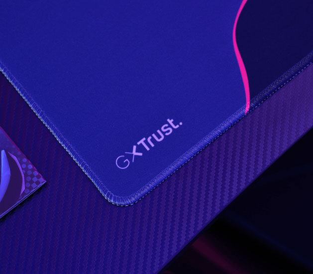 Detalle del mousepad Trust GXT en azul y violeta con bordes cosidos y logo GXT Trust en la esquina.