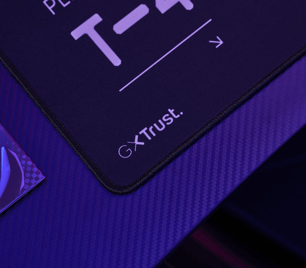 Detalle del mousepad Trust GXT en rojo y negro con bordes cosidos y logo GXT Trust en la esquina.