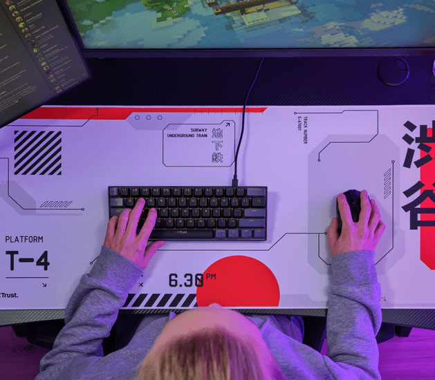 Vista superior de un escritorio con mousepad Trust GXT 759 XXL blanco y rojo, teclado y mouse, con una persona usando ambos periféricos.