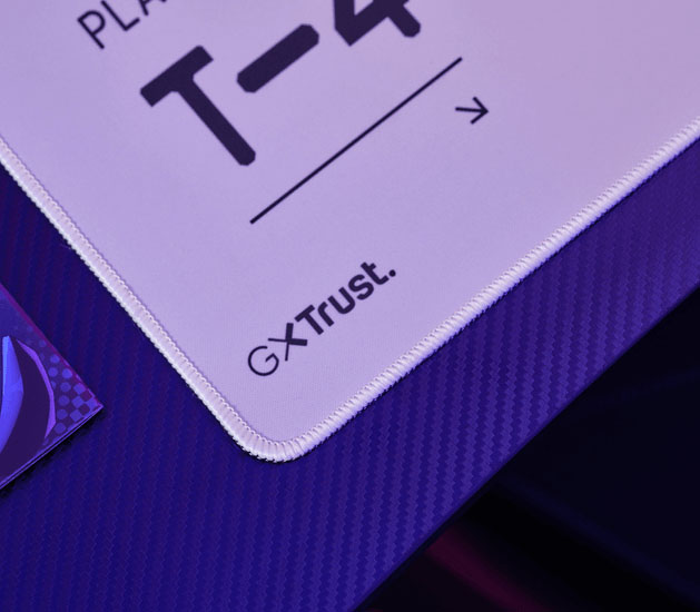 Detalle del mousepad Trust GXT en blanco y rojo con bordes cosidos y logo GXT Trust en la esquina.
