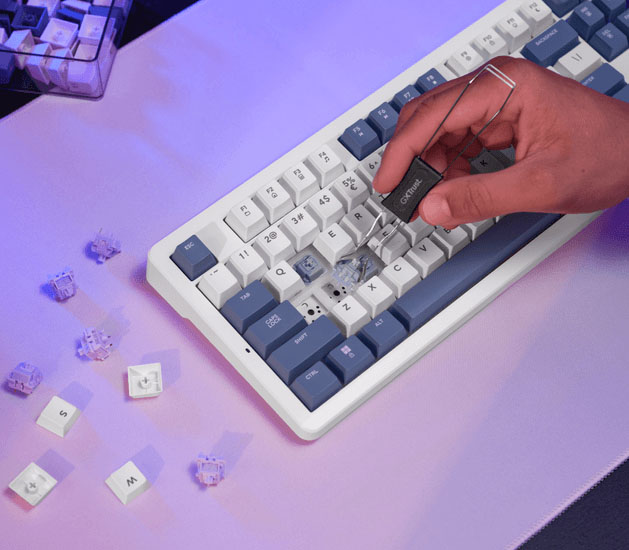 Mano usando un extractor para remover una tecla de un teclado mecánico Trust GXT 872 Xyra TKL, con keycaps y switches sueltos alrededor