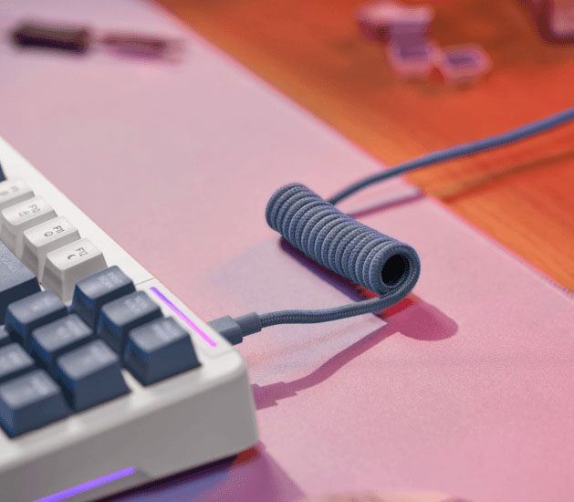 Detalle del cable trenzado con tramo en espiral conectado al teclado Trust GXT 872 Xyra TKL sobre un mousepad