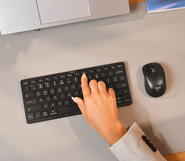 Persona usando el teclado Trust Nado II Bluetooth compacto junto a un mouse Trust en un escritorio